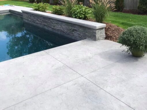 Finished landscape around a concrete pool patio with a raised stone spa wall