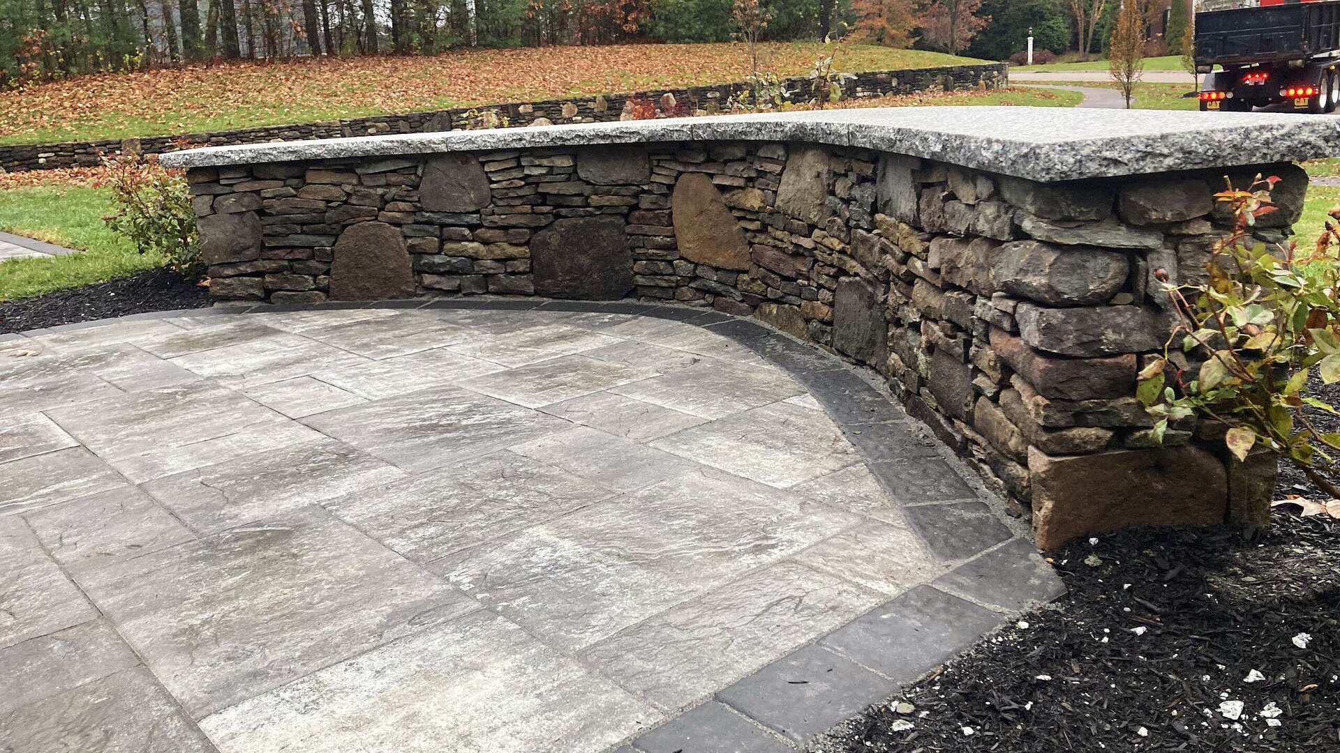 Custom paver patio with a fieldstone seat wall built by Ten Four Landscape Construction in Wrentham, MA