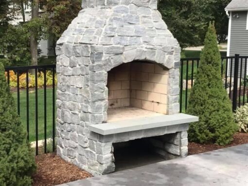 Gray stone outdoor fireplace with a bluestone hearth