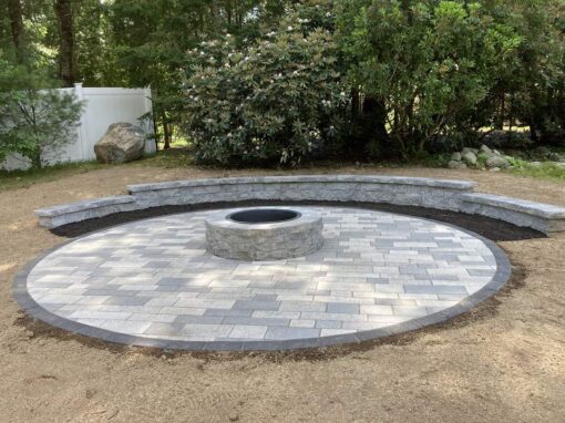 Round paver patio with a stone fire pit and curved seat wall