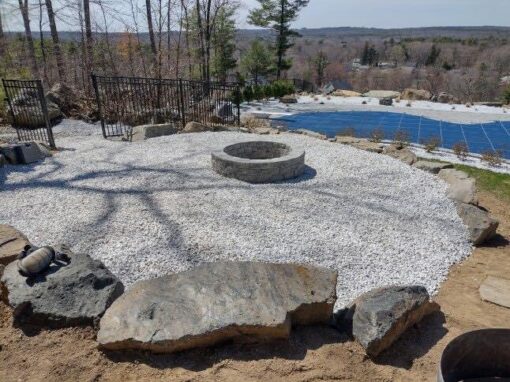 Gravel fire pit circle with boulder seating above a pool, one of our outdoor firepits
