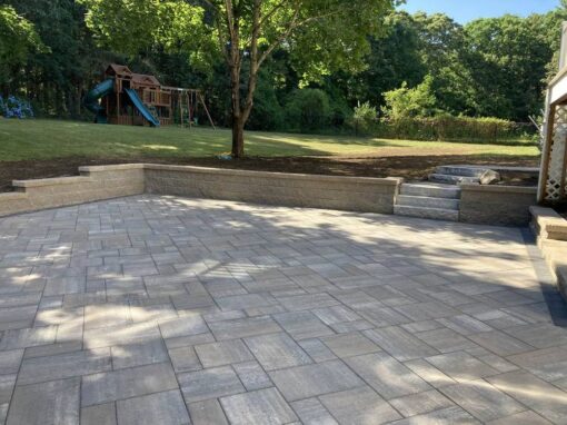 Large paver patio with a sitting wall and steps up to the backyard