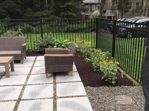 Large square pavers with gravel joints and lounge seating beside a black fence