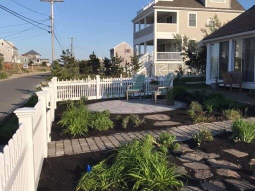 Coastal garden bed with ornamental grasses and stepping stones inside a picket fence