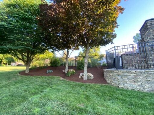 Edged mulch bed with trees along a stacked-stone pool wall