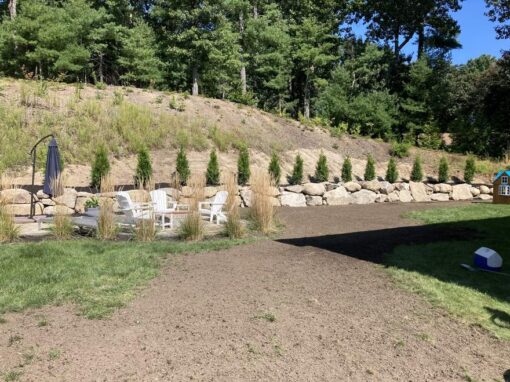 Boulder retaining wall topped with arborvitae above a regraded backyard