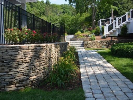 Dry-stacked natural stone retaining wall and flower bed beside a cobblestone path
