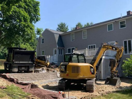 Backyard sitework with an excavator and dump truck beside the house