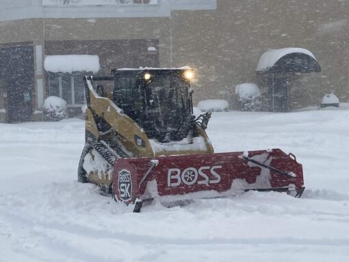 Skid steer with a snow pusher clearing a commercial parking lot