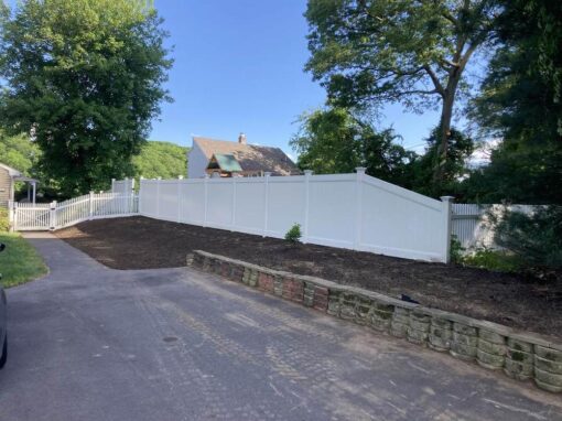 Mulch edging along a driveway bed with a block wall and vinyl fence
